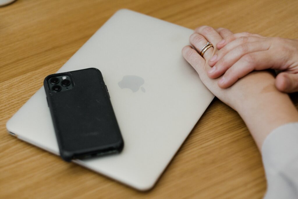 Smartphone und gefaltete Hände liegen auf einem geschlossenen Macbook
